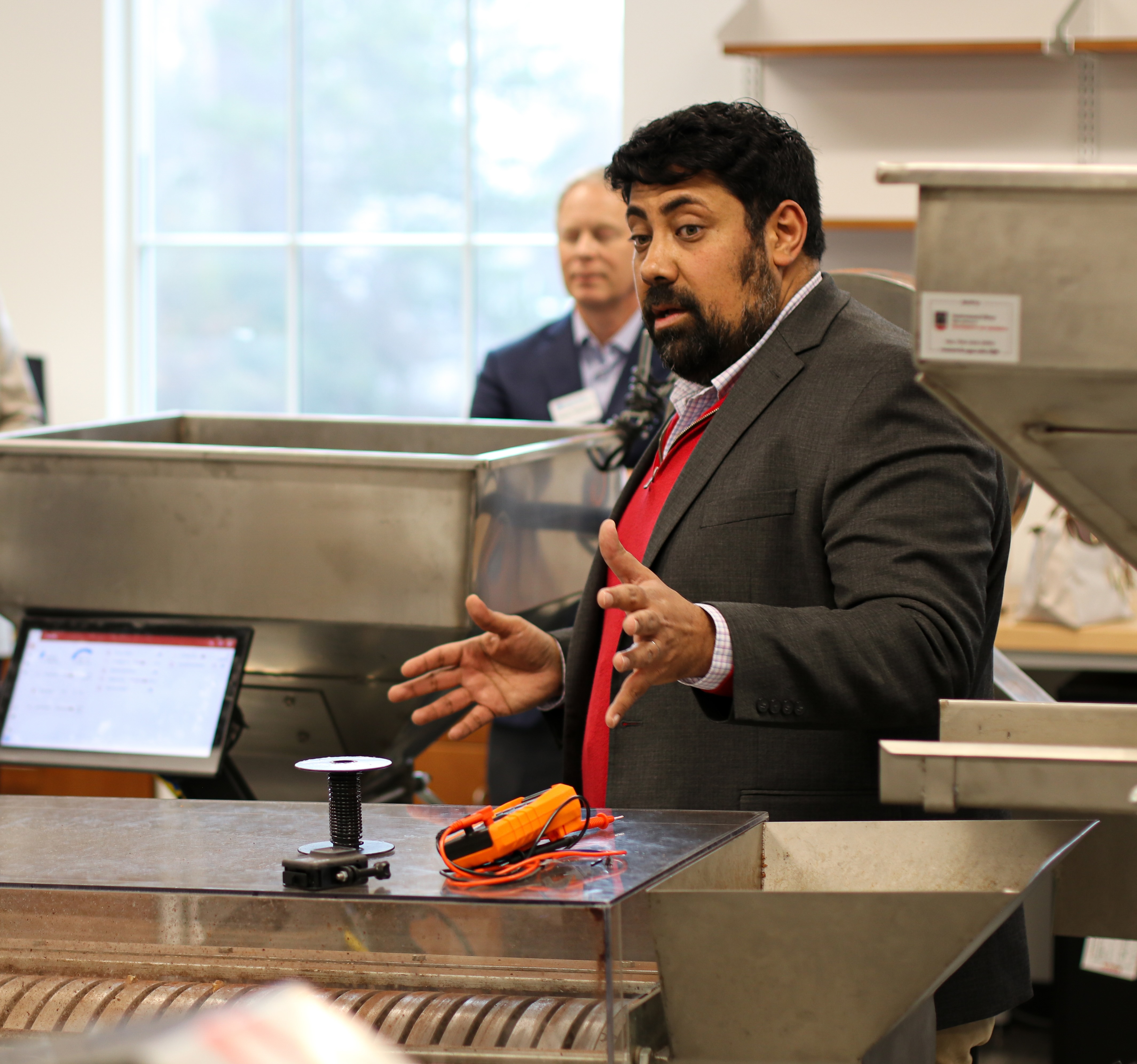 Dr. Morkos speaking to a group of people while standing by a large machine.